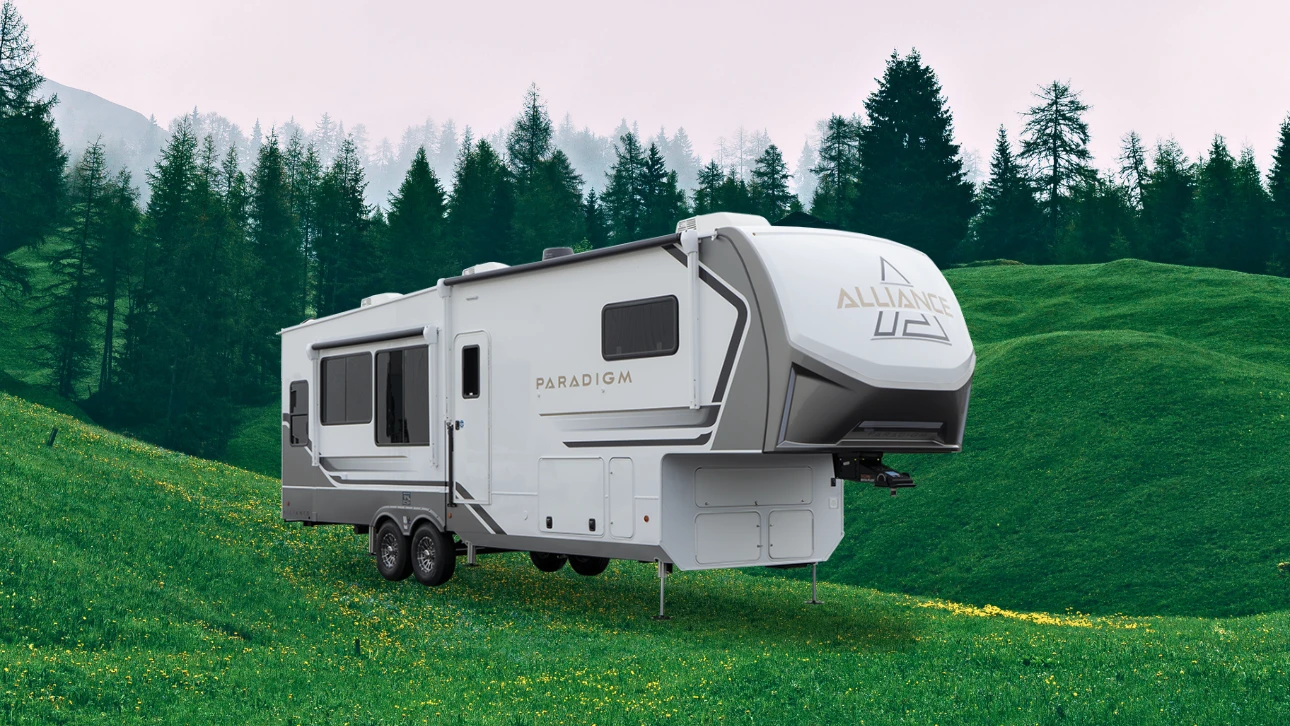 Roulotte Alliance Paradigm stationnée sur un terrain verdoyant entouré d’arbres et de collines, représentant une marque haut de gamme de VR 2025.