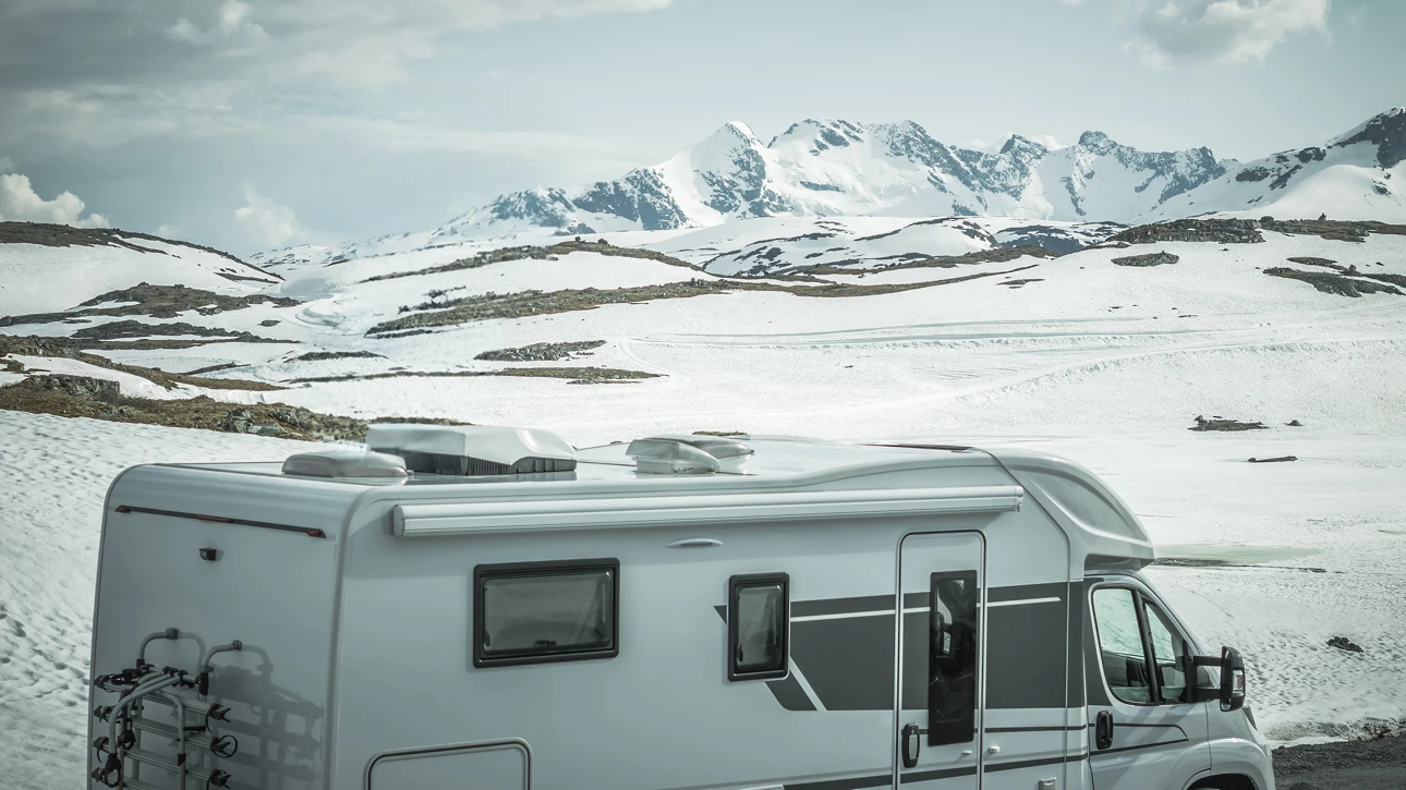 Roulotte blanche stationnée dans un paysage enneigé avec montagnes en arrière-plan, illustrant la préparation et l’hivernisation d’un VR pour la saison froide.