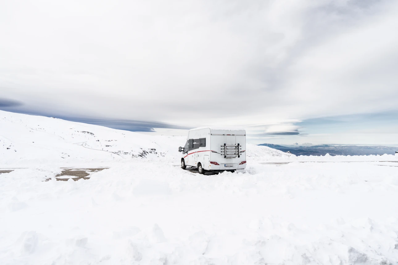 Roulotte blanche stationnée seule dans un vaste paysage enneigé, symbolisant l’hivernisation complète d’un VR avant la saison froide.
