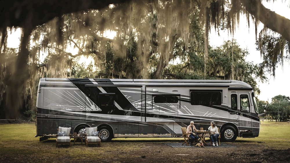 Motorisé Entegra de luxe stationné sous un grand arbre avec des campeurs assis autour d’une table, représentant l’élégance et le confort haut de gamme.