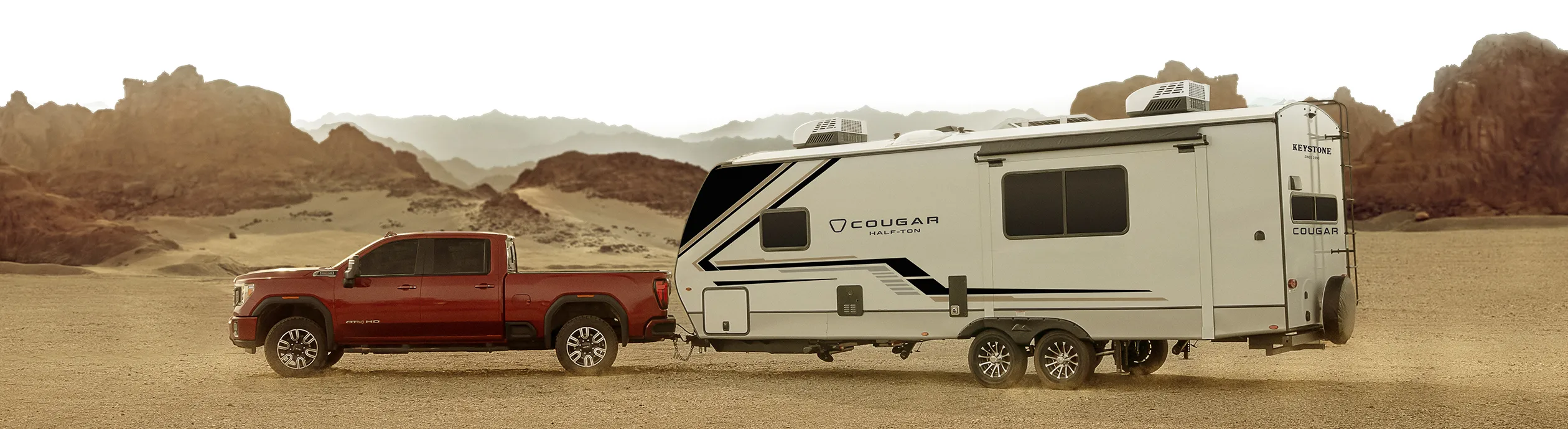 Camion rouge remorquant une roulotte Keystone Cougar dans un paysage désertique, illustrant la puissance et la fiabilité des modèles 2025.